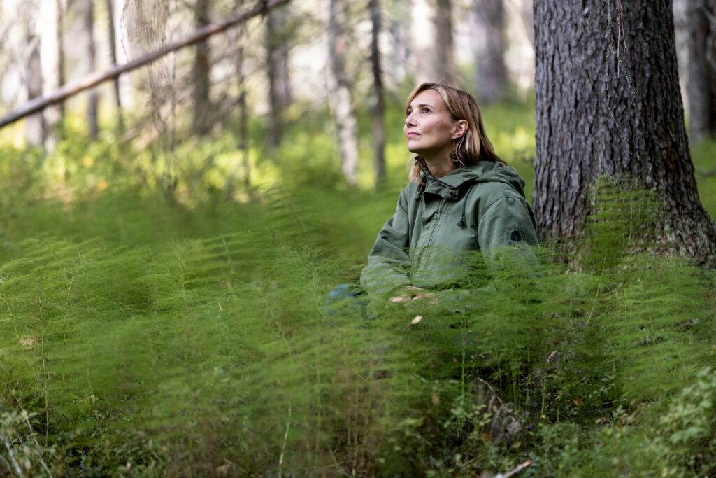 Kirjailija Jenni Räinä korkeiden vihreiden kortteiden keskellä.