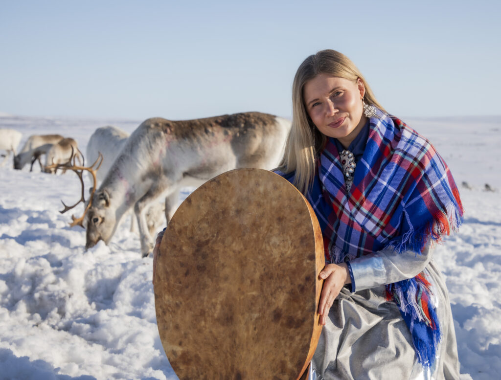 Kuvassa Ingá-Máret Gaup-Juuso rumpu kädessä ja poroja taustalla talvisessa maisemassa.