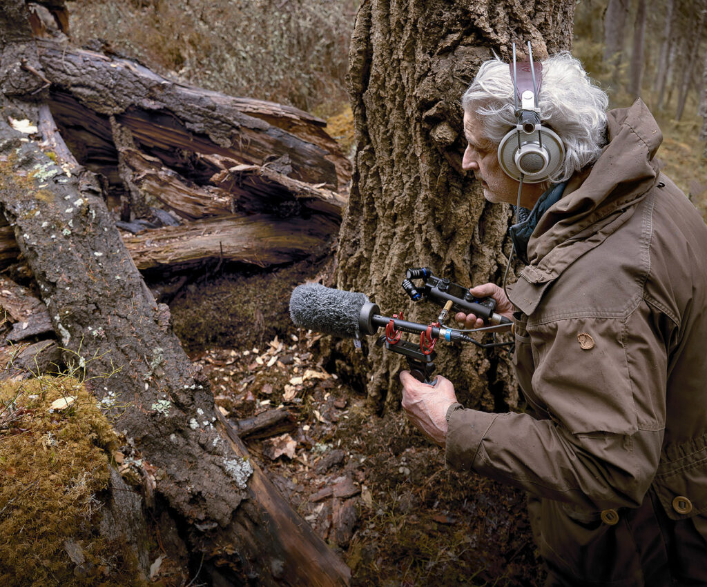 Valokuvataiteilija Taneli Eskola äänittää metsän ääniä puiden katveessa.